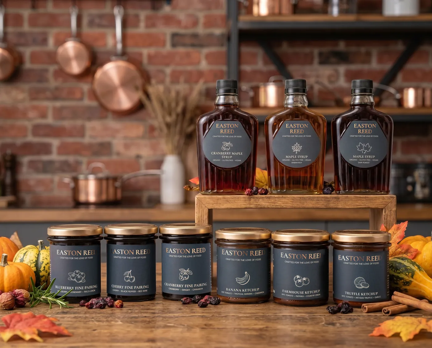 Three Easton Reed organic maple syrups on a wooden stand above Fine Pairings jars and Banana, Farmhouse and Truffle Ketchup in a brick kitchen